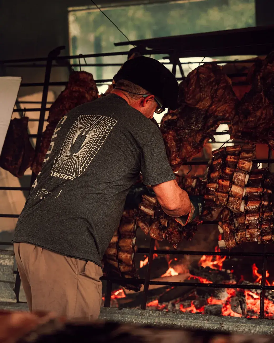 Cocinero atendiendo la parrilla cargada de carne sobre las brasas