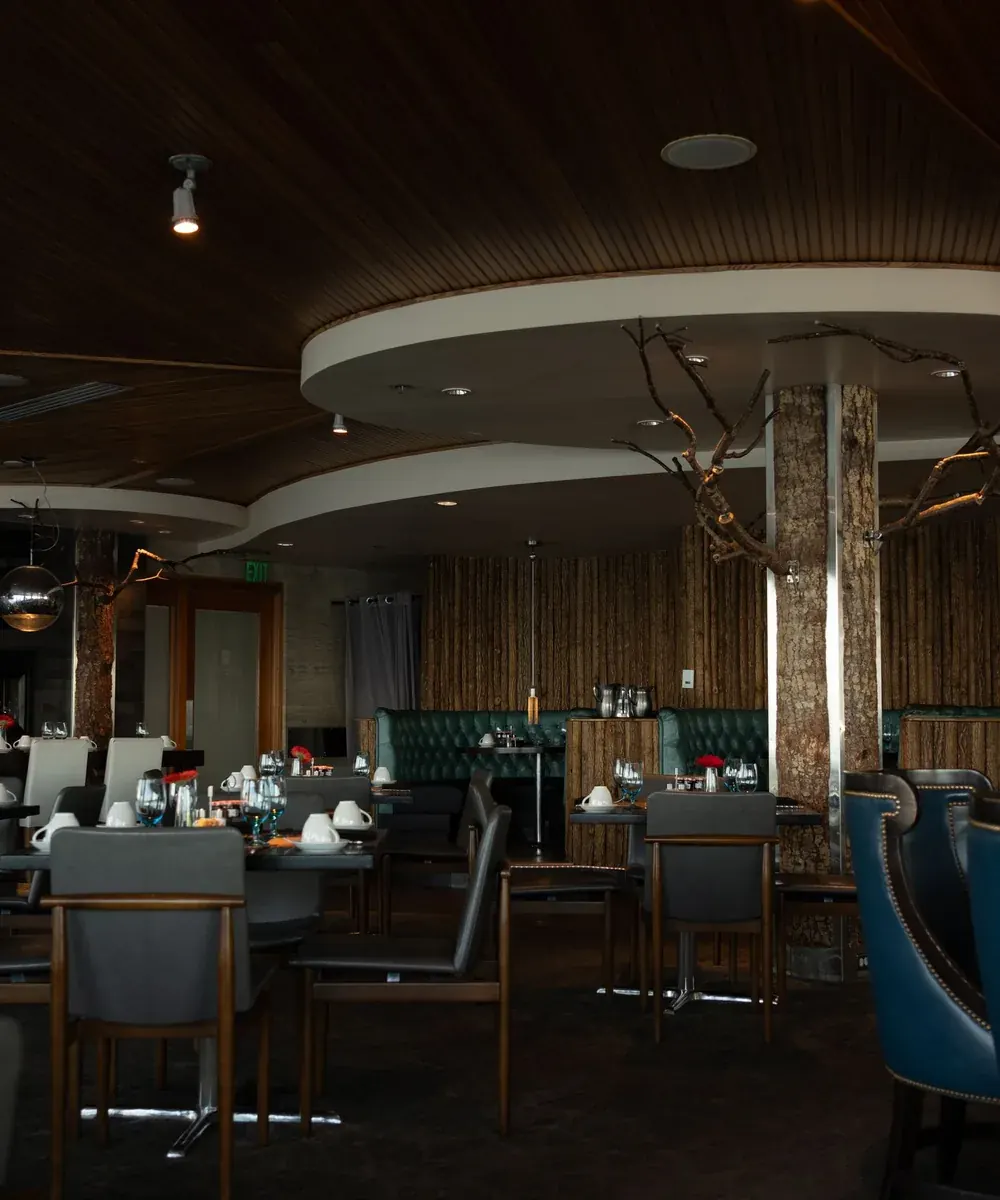 Comedor de Rescoldo con luz baja, columnas de madera y banquetas verdes